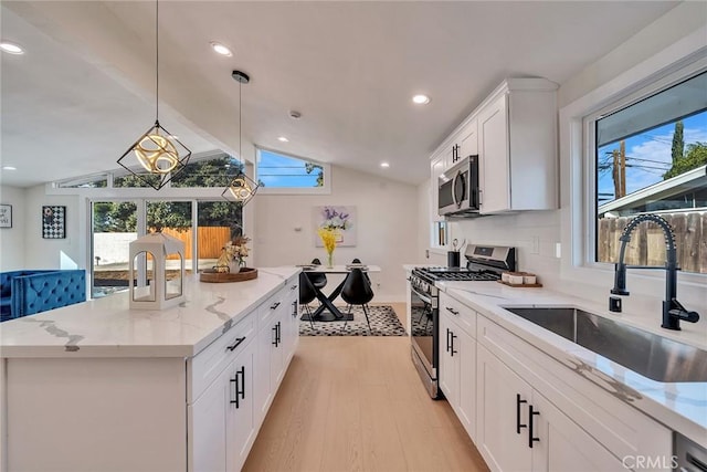 kitchen with sink, hanging light fixtures, a kitchen island, stainless steel appliances, and white cabinets