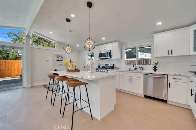 kitchen with sink, decorative light fixtures, an island with sink, stainless steel appliances, and white cabinets