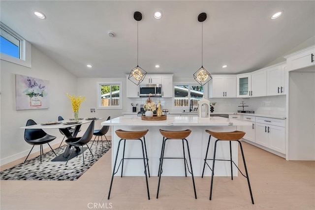 kitchen with lofted ceiling, a center island, hanging light fixtures, white cabinets, and backsplash