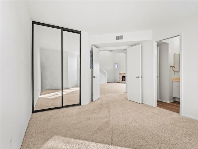 unfurnished bedroom with a brick fireplace, light colored carpet, connected bathroom, and a closet