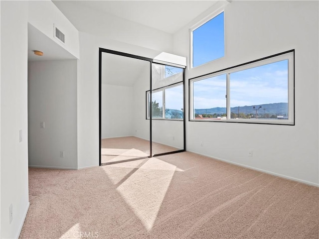 unfurnished bedroom featuring a closet, a mountain view, high vaulted ceiling, and light carpet