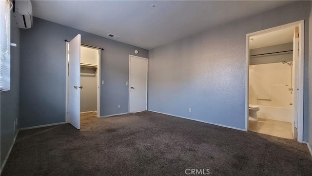 unfurnished bedroom with a wall mounted air conditioner, ensuite bath, a closet, and dark colored carpet