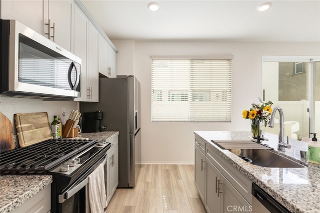 kitchen featuring sink, white cabinetry, stainless steel appliances, light stone countertops, and light hardwood / wood-style floors