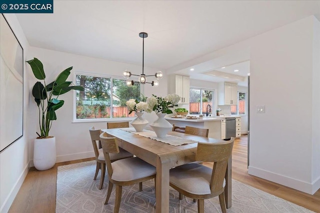 dining space with an inviting chandelier, sink, and light wood-type flooring