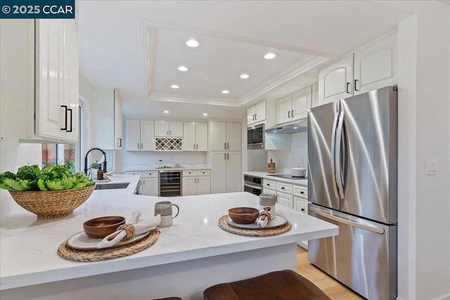 kitchen featuring wine cooler, sink, white cabinetry, appliances with stainless steel finishes, and a tray ceiling