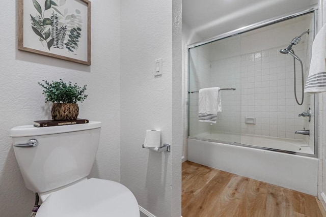 bathroom featuring hardwood / wood-style flooring, toilet, and combined bath / shower with glass door