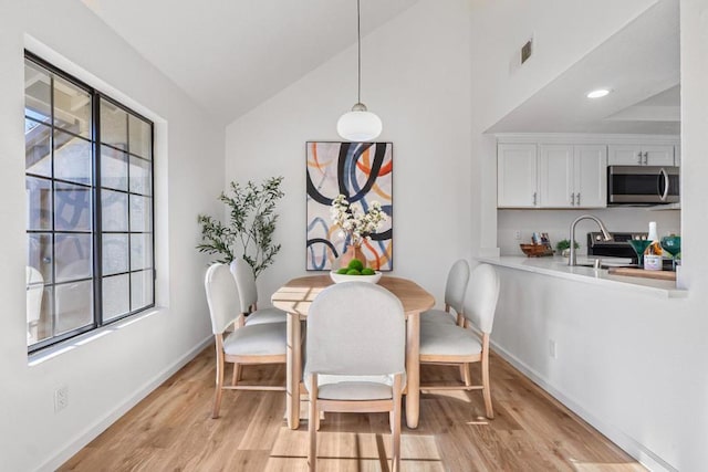 dining room with a healthy amount of sunlight, vaulted ceiling, and light wood-type flooring