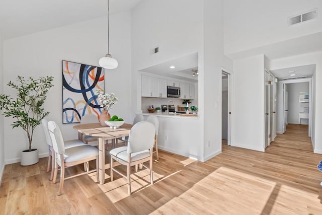 dining area with sink, a towering ceiling, and light hardwood / wood-style floors