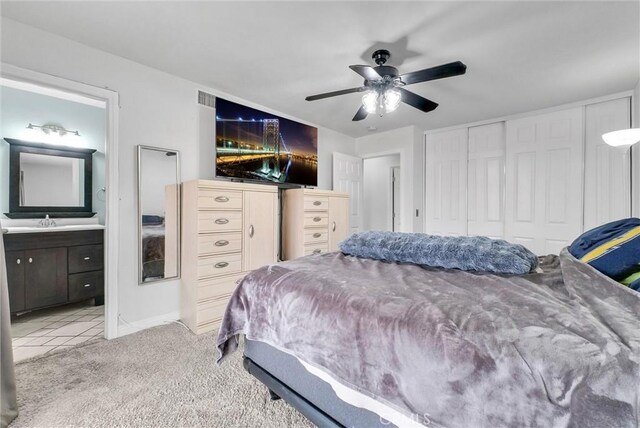 bedroom with connected bathroom, sink, light colored carpet, a closet, and ceiling fan