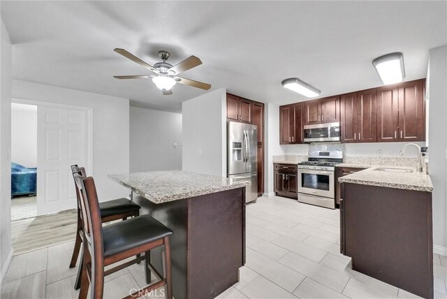 kitchen with a kitchen bar, sink, ceiling fan, stainless steel appliances, and light stone countertops