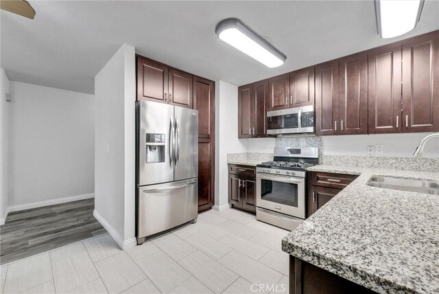 kitchen with stainless steel appliances, light stone countertops, and sink