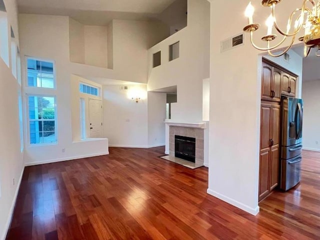 unfurnished living room with an inviting chandelier, a towering ceiling, dark hardwood / wood-style floors, and a tile fireplace