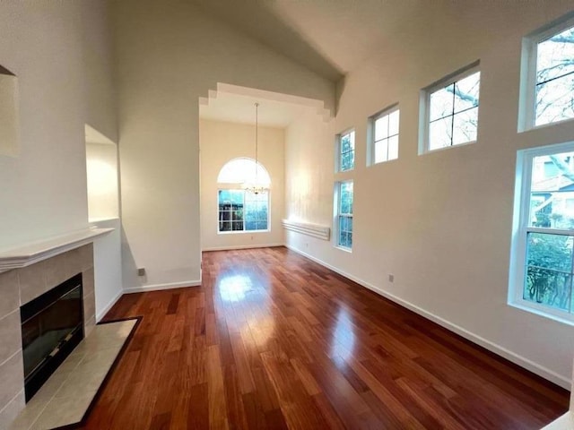 unfurnished living room with a notable chandelier, hardwood / wood-style flooring, a fireplace, and high vaulted ceiling