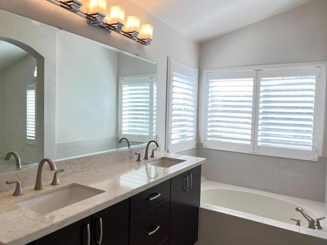 bathroom featuring tiled tub, vanity, and vaulted ceiling