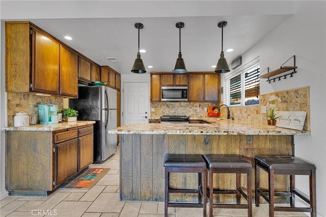 kitchen with hanging light fixtures, appliances with stainless steel finishes, kitchen peninsula, light stone countertops, and decorative backsplash