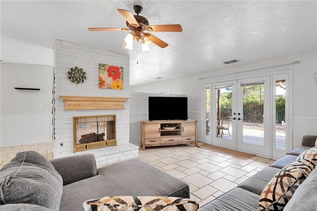 living room featuring french doors, lofted ceiling, a textured ceiling, ceiling fan, and a fireplace