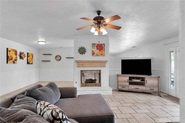 living room with ceiling fan, a fireplace, and a textured ceiling