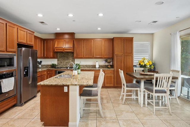 kitchen featuring sink, a center island with sink, a kitchen breakfast bar, stainless steel appliances, and light stone countertops