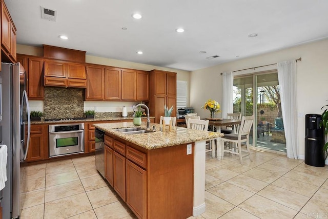 kitchen featuring light tile patterned flooring, sink, light stone countertops, a kitchen island with sink, and black appliances