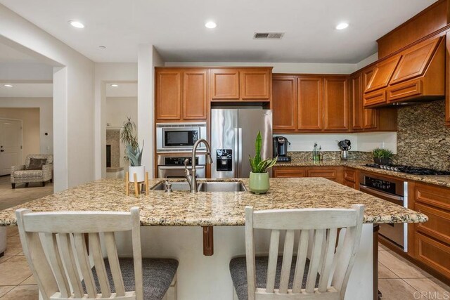 kitchen with light stone counters, sink, stainless steel appliances, and a center island with sink