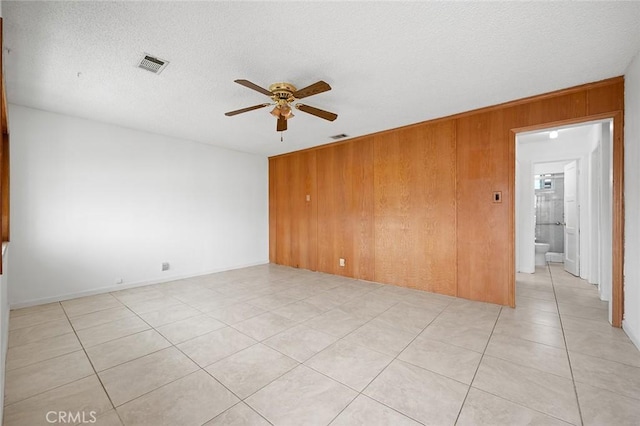 tiled empty room with ceiling fan, wooden walls, and a textured ceiling