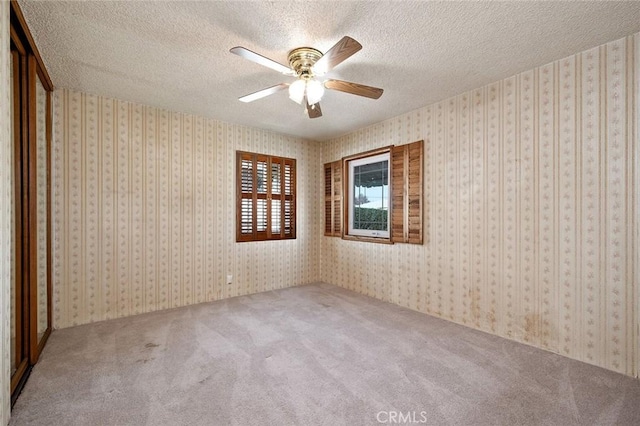 empty room featuring ceiling fan, a textured ceiling, and carpet