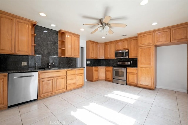 kitchen with appliances with stainless steel finishes, tasteful backsplash, dark stone countertops, light tile patterned floors, and ceiling fan