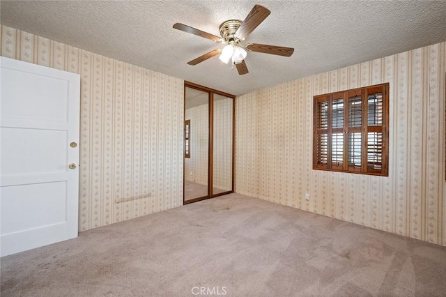 unfurnished bedroom with ceiling fan, a closet, a textured ceiling, and carpet flooring