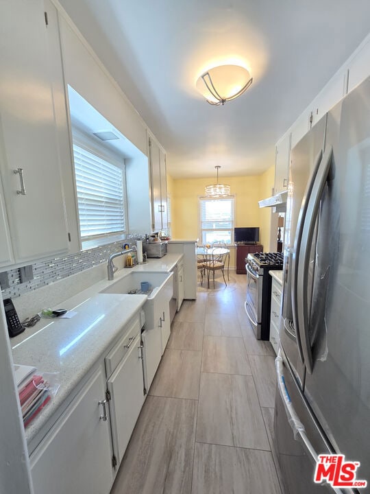 kitchen with tasteful backsplash, white cabinets, a chandelier, hanging light fixtures, and stainless steel appliances