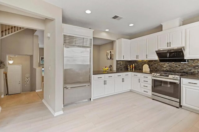 kitchen featuring decorative backsplash, range hood, white cabinets, and appliances with stainless steel finishes