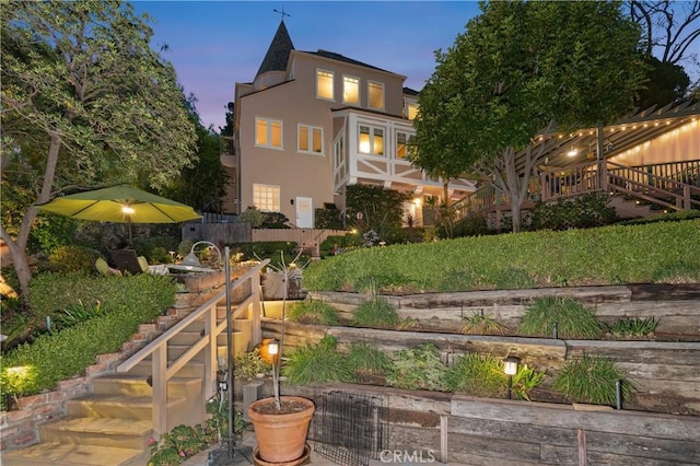 back of house at dusk featuring stucco siding, fence, and stairs