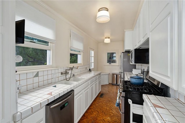 kitchen with tile counters, white cabinets, stainless steel appliances, and a sink