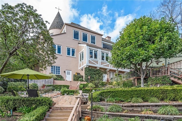 rear view of property featuring a chimney, fence, stairway, and stucco siding