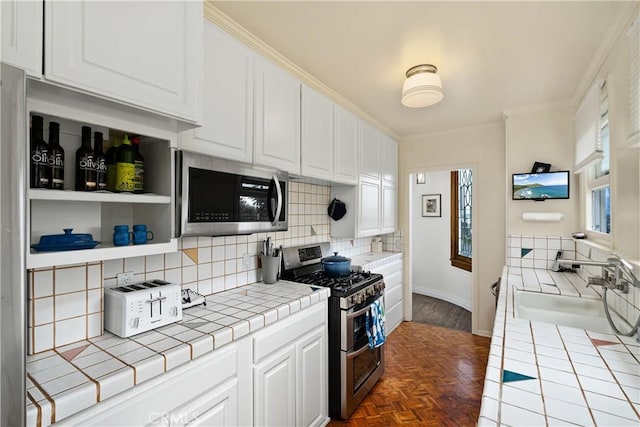 kitchen with decorative backsplash, white cabinets, tile countertops, appliances with stainless steel finishes, and a sink