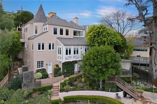 rear view of house featuring a chimney, fence, stairway, and stucco siding