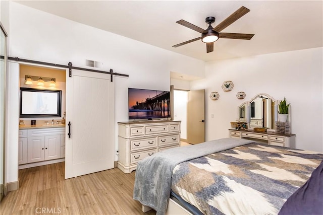 bedroom with sink, connected bathroom, a barn door, and light hardwood / wood-style floors