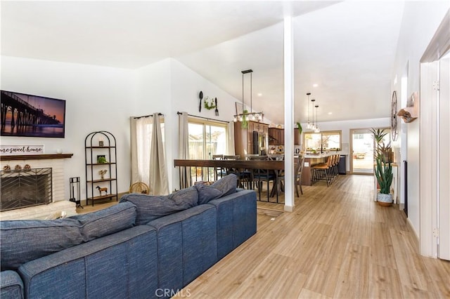 living room with lofted ceiling, a brick fireplace, and light hardwood / wood-style floors