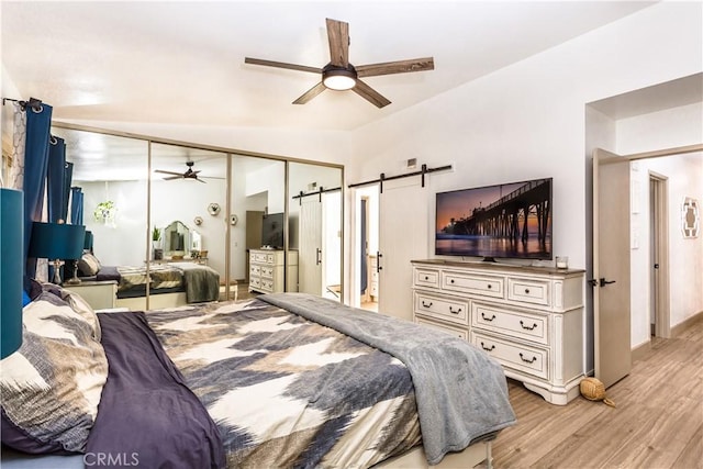 bedroom featuring a closet, a barn door, ceiling fan, and light wood-type flooring