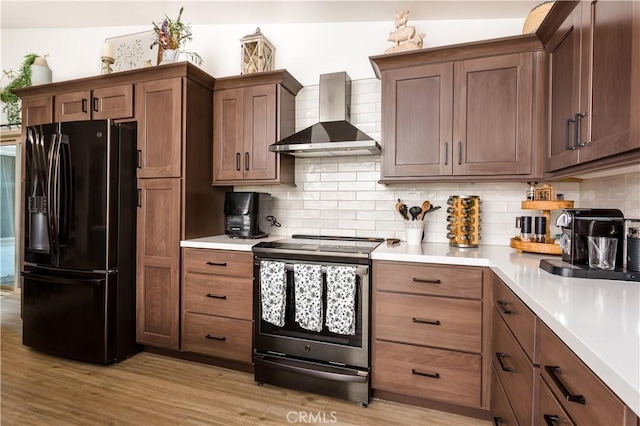 kitchen with tasteful backsplash, wall chimney exhaust hood, light hardwood / wood-style floors, black refrigerator with ice dispenser, and electric stove