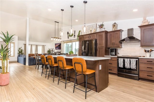 kitchen with wall chimney range hood, hanging light fixtures, a kitchen island, stainless steel appliances, and a kitchen bar