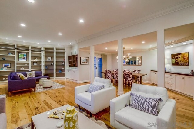 living room with a notable chandelier, ornamental molding, and light wood-type flooring