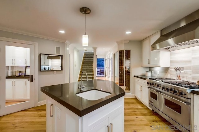 kitchen with white cabinetry, sink, wall chimney range hood, and range with two ovens