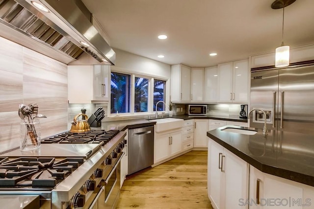 kitchen with range hood, sink, white cabinets, hanging light fixtures, and stainless steel appliances