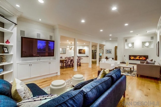 living room with ornate columns, ornamental molding, an inviting chandelier, and light hardwood / wood-style flooring