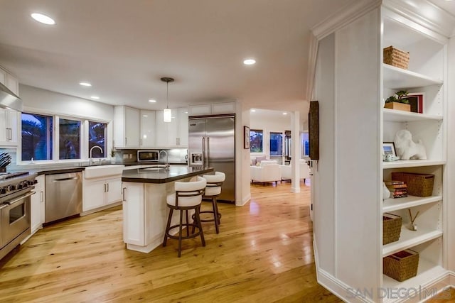 kitchen with a breakfast bar, white cabinetry, high end appliances, a kitchen island, and decorative light fixtures