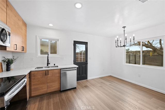 kitchen with pendant lighting, sink, stainless steel appliances, tasteful backsplash, and light wood-type flooring