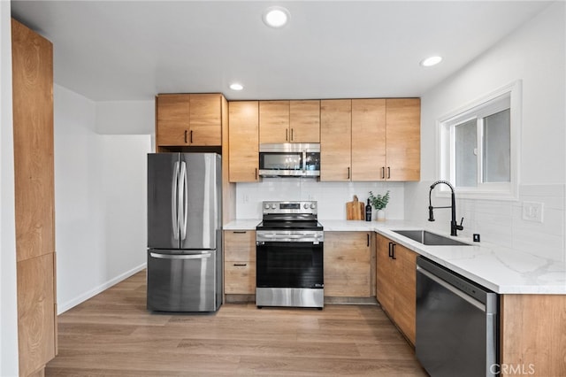 kitchen with appliances with stainless steel finishes, sink, light stone counters, and light hardwood / wood-style floors