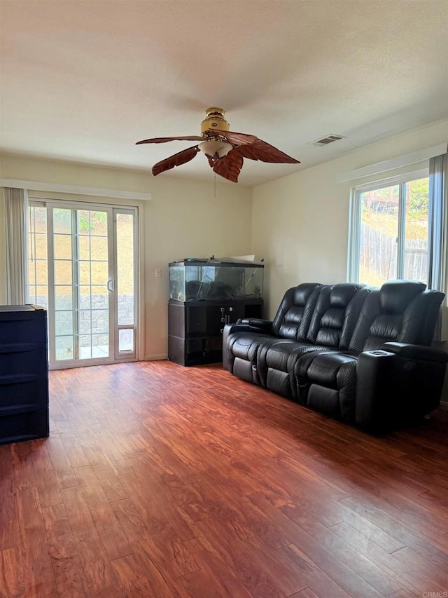 living area featuring a ceiling fan, a healthy amount of sunlight, visible vents, and wood finished floors