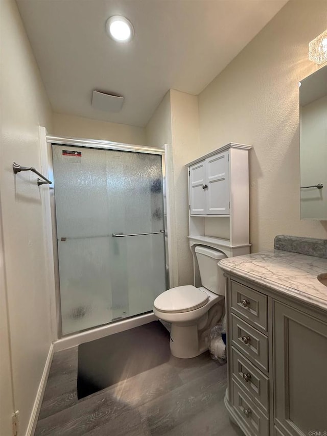 full bathroom featuring toilet, a shower stall, vanity, wood finished floors, and baseboards