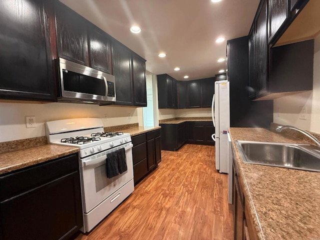 kitchen with recessed lighting, light wood-style floors, a sink, dark cabinets, and white appliances